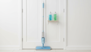 Sleek spray mop hanging on a pantry door with two refillable bottles of blue and green cleaning solution beside it. Best quick floor cleaning solution for apartments