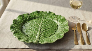 Bright green 11-inch cabbage leaf stoneware plate on a linen tablecloth with gold flatware and a wine glass in warm sunlight.