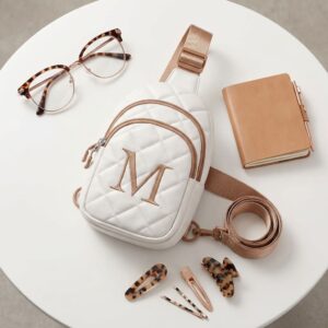 Pastel pink YOOLIFE initial crossbody bag displayed on a white table beside sunglasses, hair clips, and a small notebook.