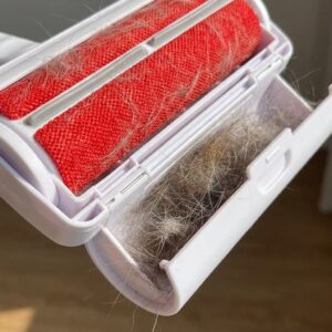 Close-up of the 1ABOVE pet hair remover showing its micro-bristle roller strip and pop-open waste compartment filled with collected pet fur.